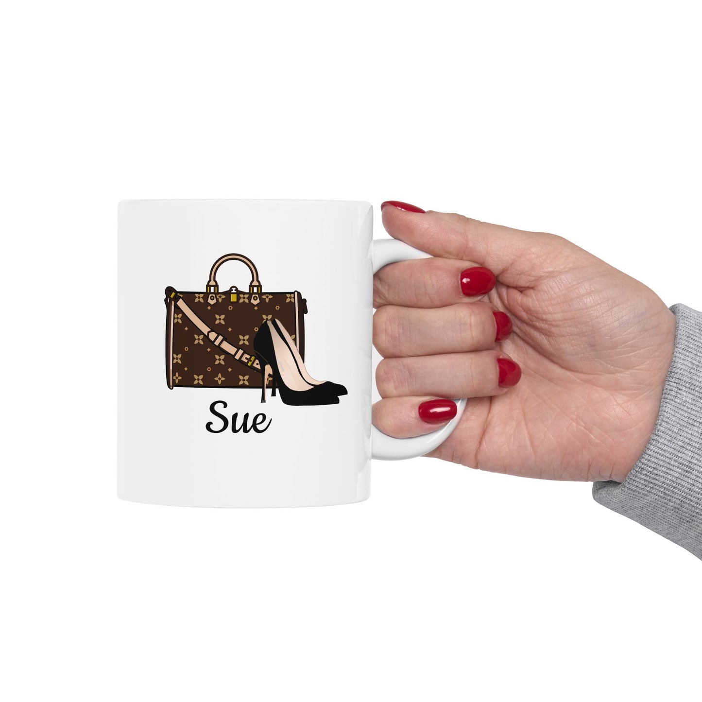 White mug with a handbag and shoe design, held by a hand with red nails on a white background.