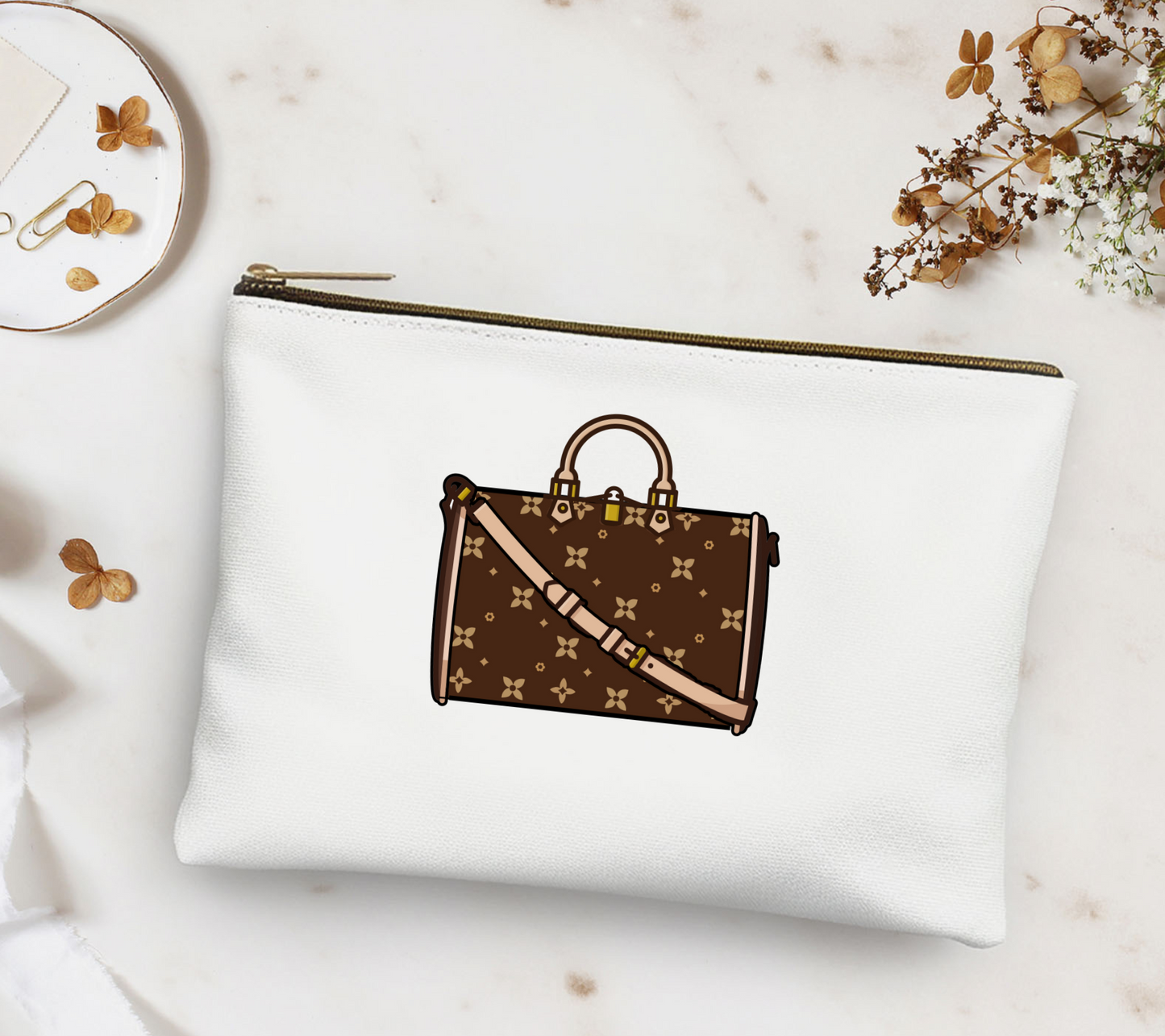 White pouch with brown handbag design on a marble surface with flowers and a plate.