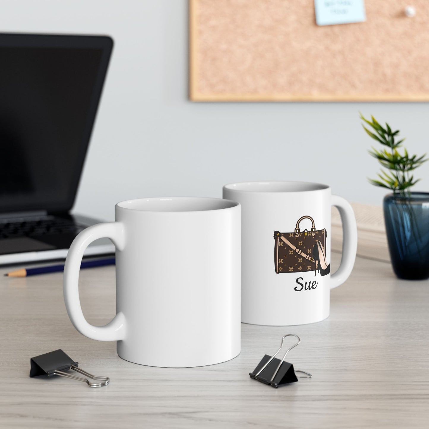 Two white mugs with personalized designs on a desk with office supplies.