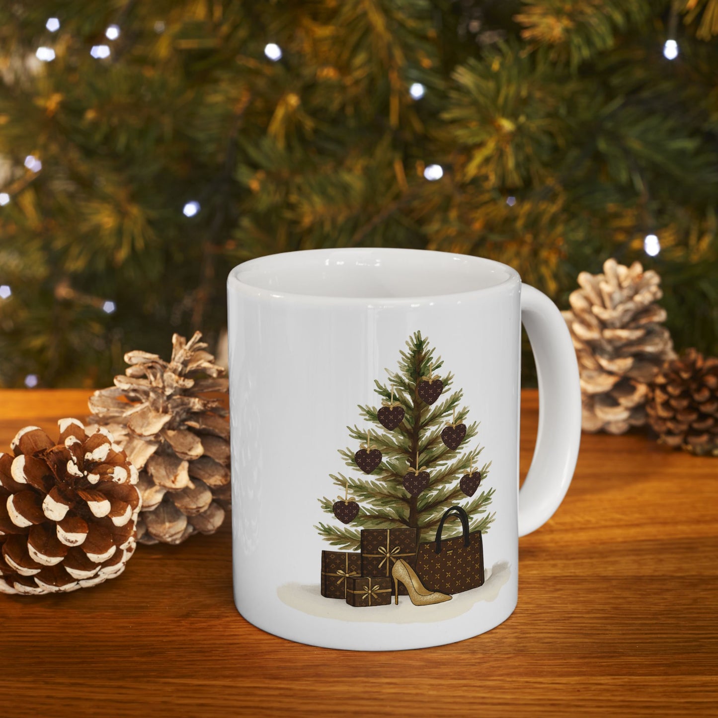 White mug with Christmas tree and gift design on a wooden table with pinecones and a blurred Christmas tree in the background.
