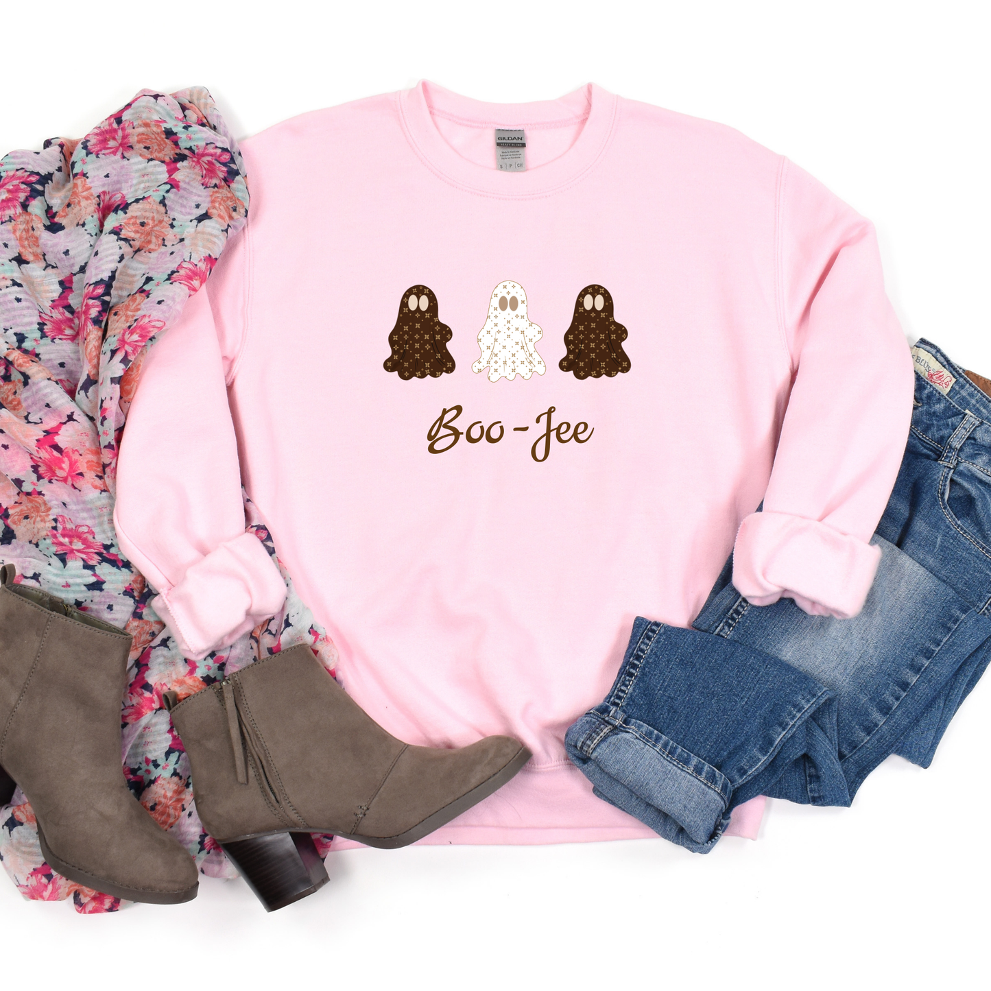 Pink sweatshirt with ghost design and 'Boo-Jee' text, surrounded by floral fabric, boots, and jeans on a white background.