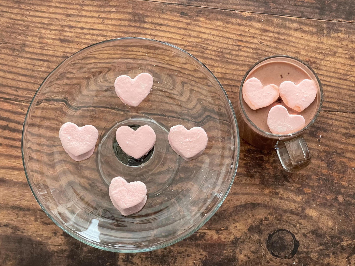 Heart-shaped pink marshmallows on a glass plate with a mug of hot chocolate.