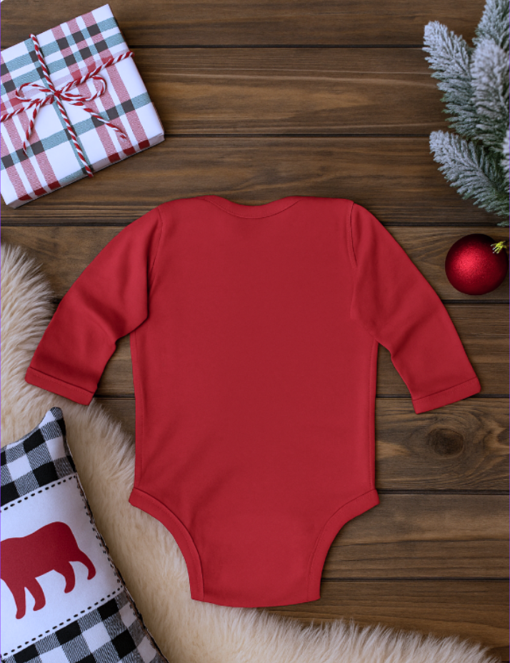 Red baby onesie on a wooden surface with a gift and Christmas decorations.