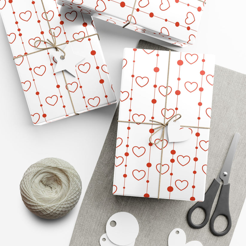 Gift wrap with heart patterns, scissors, and yarn on a white surface