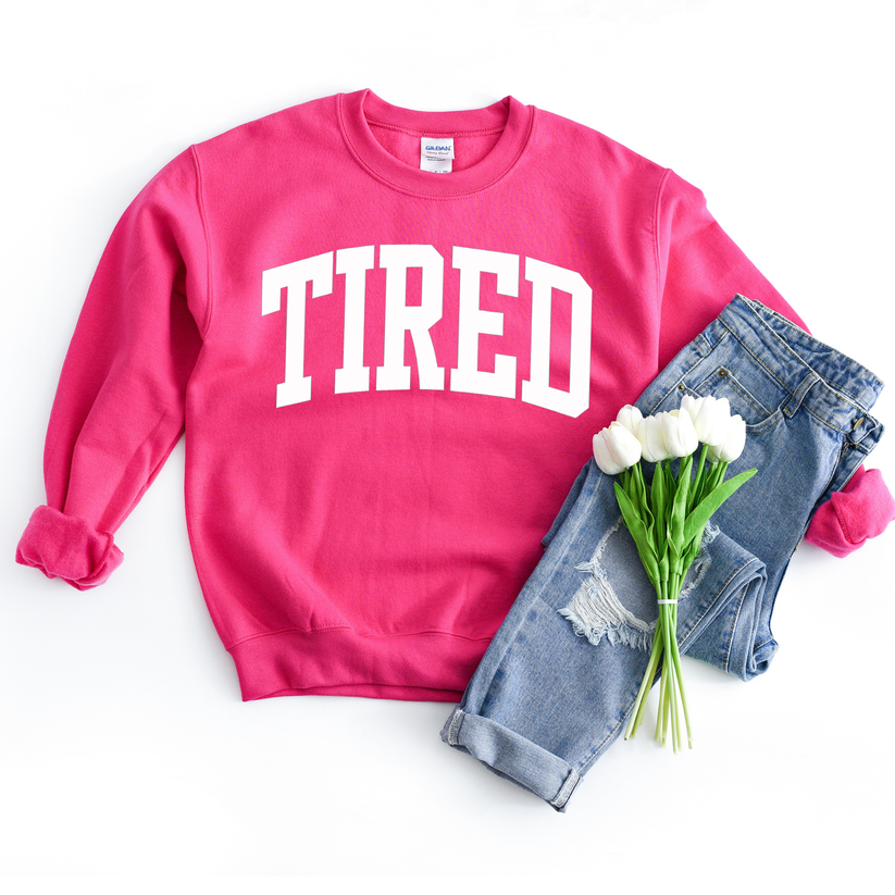 Pink sweatshirt with 'TIRED' text, denim shorts, and white flowers on a white background