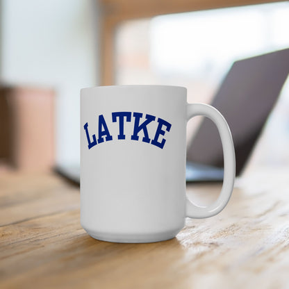 White mug with 'LATKE' printed in blue on a wooden surface.