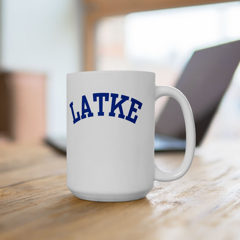White mug with 'LATKE' printed in blue on a wooden surface.