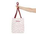 Tote bag with red heart pattern and 'Helena' text, held by a hand on a white background