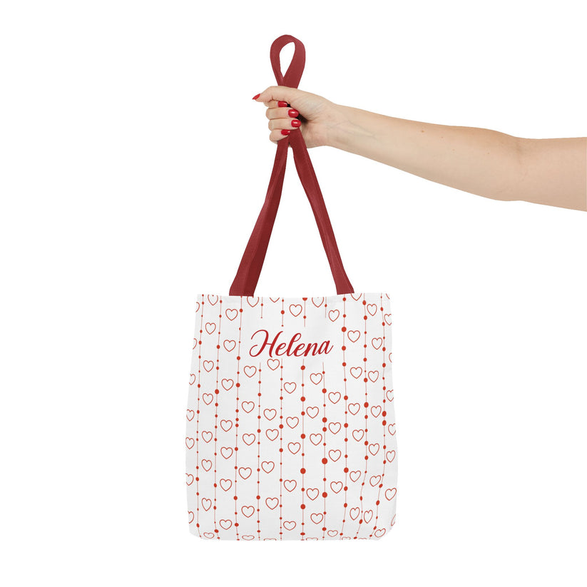 Tote bag with red heart pattern and 'Helena' text, held by a hand on a white background