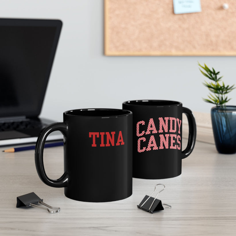 Two black mugs with 'TINA' and 'CANDY CANES' text on a desk with office supplies.