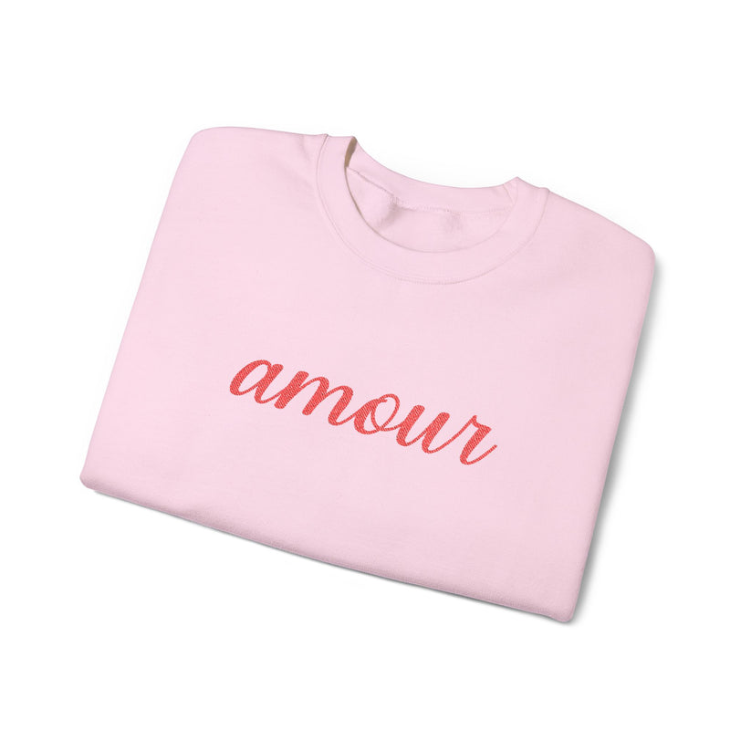 Folded pink sweatshirt with 'amour' text on a white background
