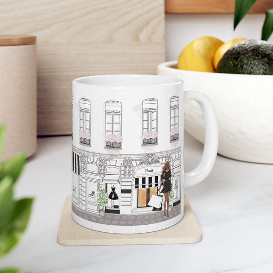 White ceramic mug from the Haute in Paris Collection featuring a chic Parisian boutique scene with a fashionable woman holding shopping bags.