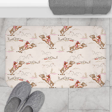 Patterned bath mat with a vintage cowgirl and bucking bronco print in pink tones.