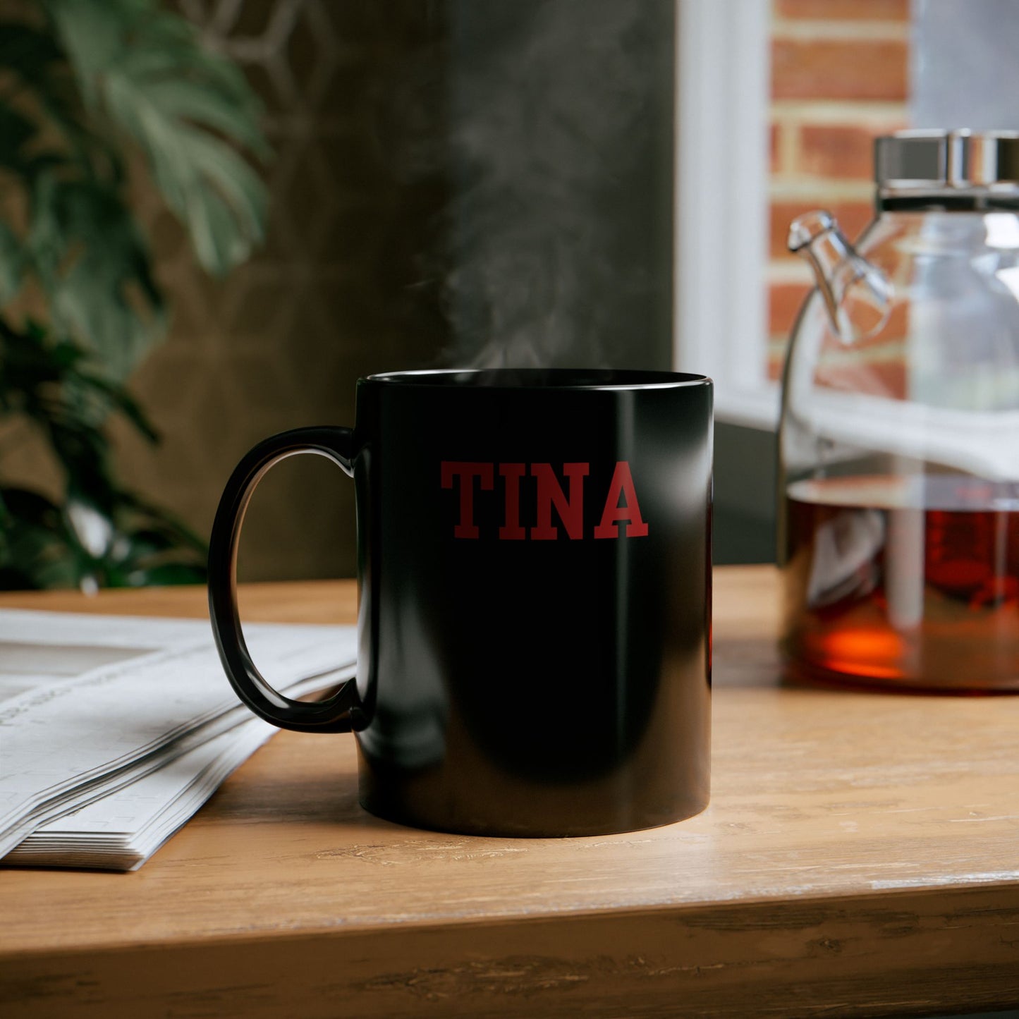 Black mug with 'TINA' in red on a wooden table with a blurred background