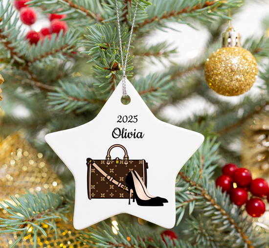 Star-shaped Christmas ornament with a handbag and high heel design, hanging on a decorated tree.