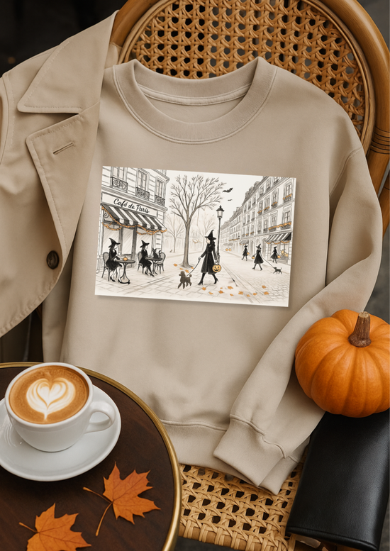 Beige sweatshirt with a printed design, placed on a chair next to a cup of coffee and a pumpkin.