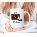 White mug with a design of a handbag and high heels, held by a person.