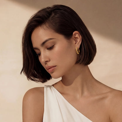 Woman wearing gold bamboo shaped hoop earrings against a beige background