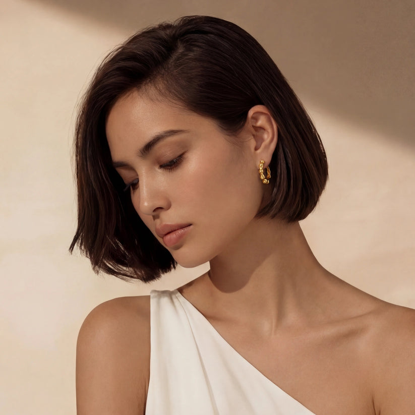 Woman wearing gold bamboo shaped hoop earrings against a beige background