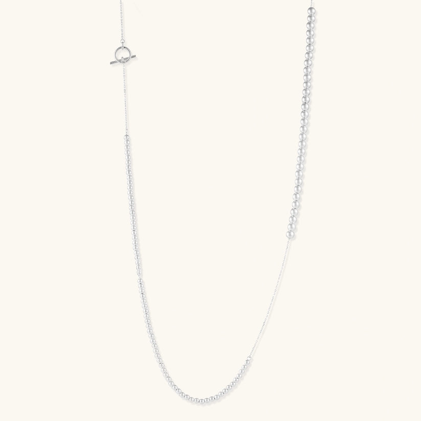 Long sterling silver beaded necklace with graduated sphere design, toggle clasp, and delicate chain extension on white background