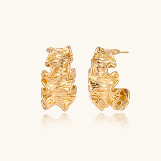 Pair of gold ruffle huggie hoops with sculpted wave texture and dimensional ripples on neutral background.