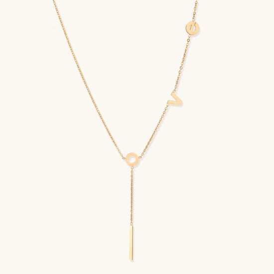 Gold necklace with the letters "love" on a light beige background
