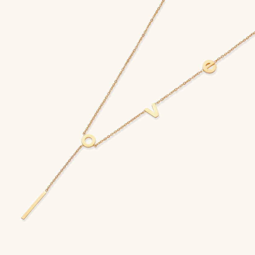 Gold necklace with letters spelling out "love" on a white background