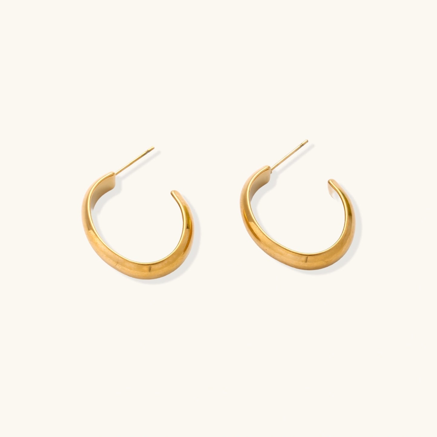 Chunky tubular hoop earrings in warm 14K gold-plated finish with smooth polished surface on cream background.