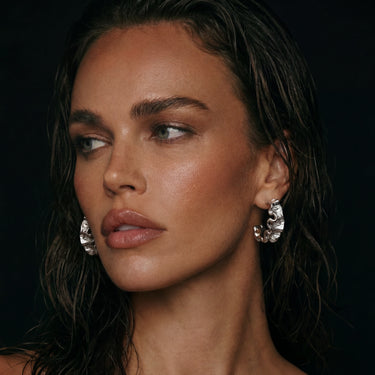 Close-up of a woman wearing white gold plated ripple wave earrings with a dark background