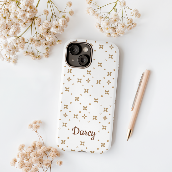 Phone case with floral pattern and 'Darcy' text on a light surface with flowers and a pen.