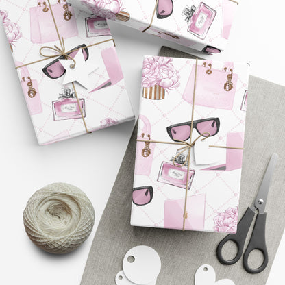 Gift wrap with pink and white design featuring sunglasses and a bottle, tied with string, on a white surface with scissors and yarn.