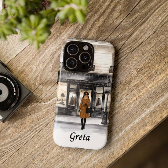 Phone case with a design of a woman in a coat and the name 'Greta' on a wooden surface.
