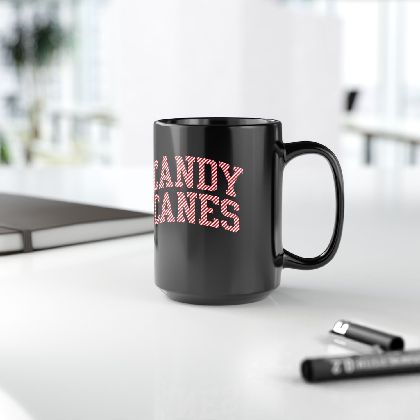 Black mug with 'CANDY CANES' text on a white surface with office items.