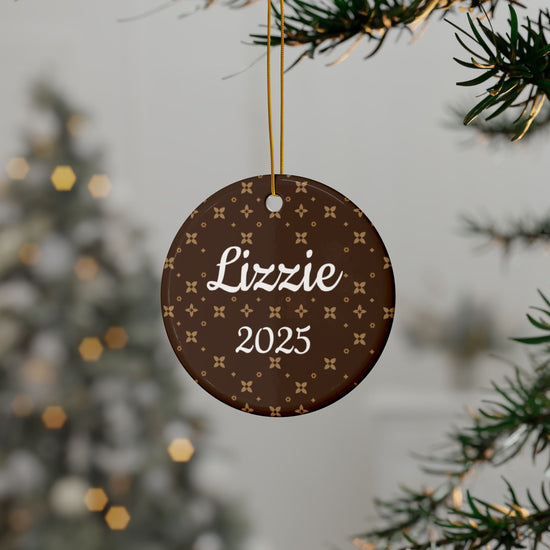 Round decorative ornament with 'Lizzie' and '2025' text, hanging on a tree branch.