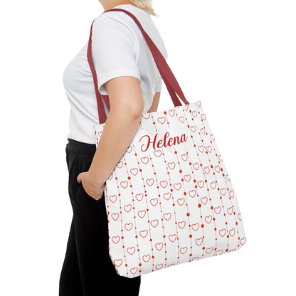 Person holding a white tote bag with red heart patterns and 'Helena' printed on it.