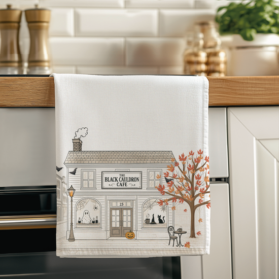 Decorative towel with a Halloween Black Cat cafe design hanging on a kitchen towel rack.