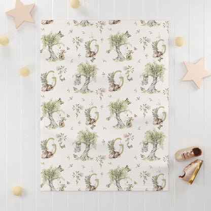 Soft plush baby blanket, cream background with watercolor illustrations of a bunny and mouse.  Shown on a white, shiplap background. Personalized with a monogram letter.