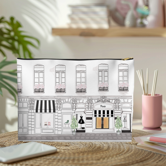 Makeup bag with Parisian shopping street design on a desk with a plant and pink cup in the background