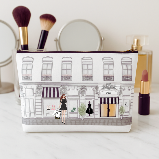 Cosmetic bag with a design of a street scene and people, placed on a surface with makeup items around.