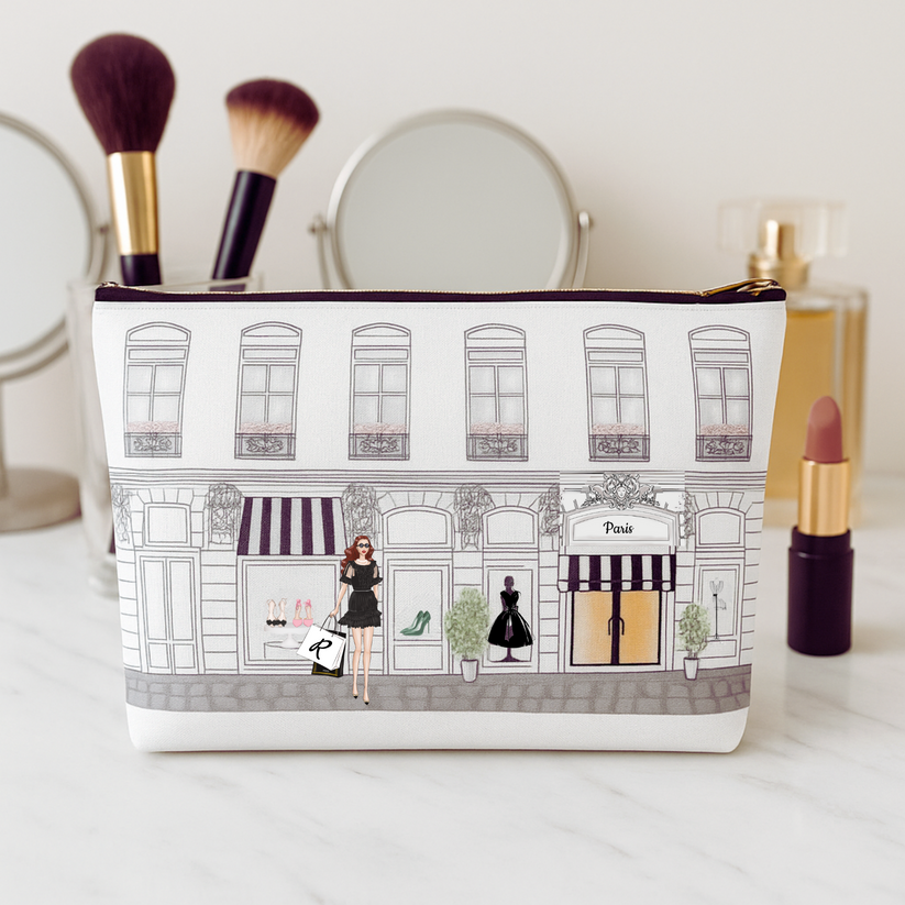 Cosmetic bag with a design of a street scene and people, placed on a surface with makeup items around.