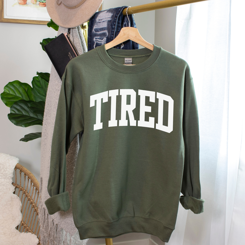 Green sweatshirt with 'TIRED' text on a hanger against a neutral background