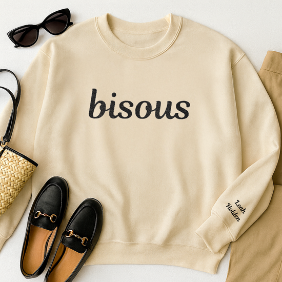 Sand colored sweatshirt with embroidered word "bisous" on the chest.  Additional text on the left sleeve.