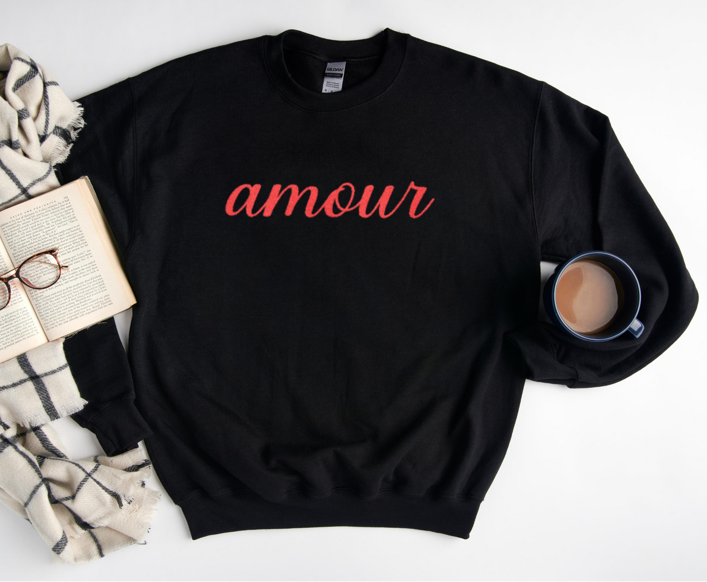 Black sweatshirt with 'amour' text on a white surface with a book and mug.