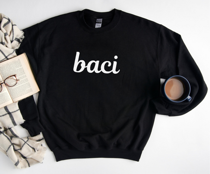 Black sweatshirt with 'baci' text on a white surface with books, glasses, and a mug.