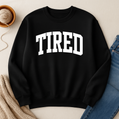 Black sweatshirt with 'TIRED' text on a neutral background