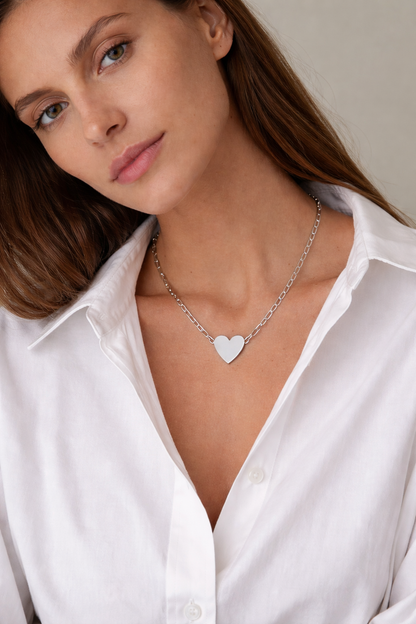 Woman wearing a silver heart necklace with a plain background