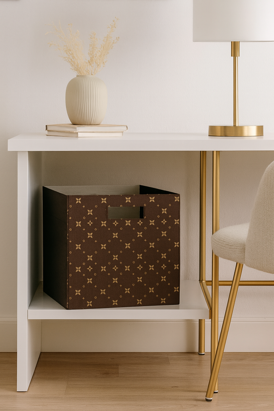 White side table with a brown patterned box, gold lamp, and books on a light wood floor.