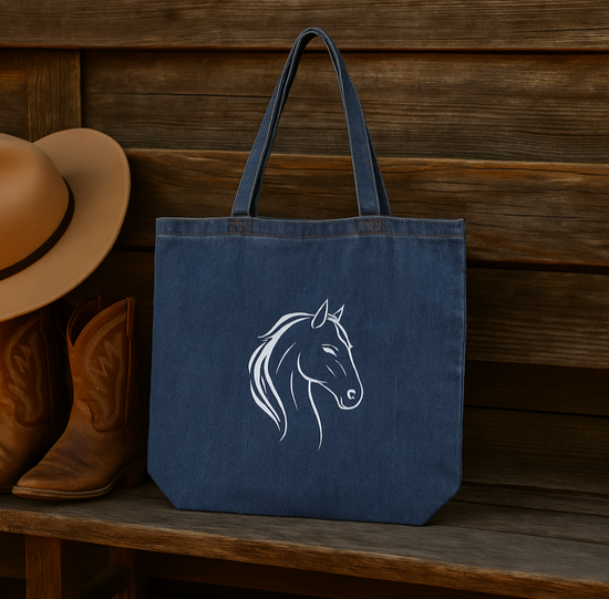 Blue denim  tote bag with horse design on a wooden surface next to cowboy boots and a hat.