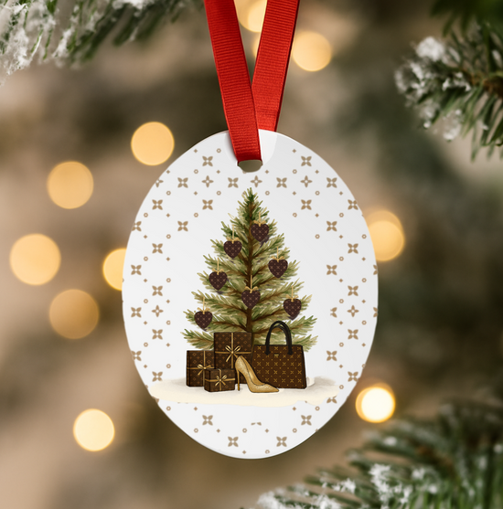 Decorative Christmas ornament with a tree, presents, and shoes on a white background, hanging from a red ribbon against a blurred Christmas tree and lights.