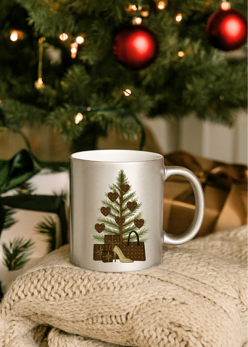 Silver mug with Christmas tree design on a textured surface with a decorated tree in the background